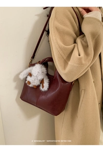 Detail of a vintage dark red bucket bag with a plush rabbit charm and shoulder strap