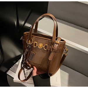 Detailed view of brown handbag featuring a heart-shaped metal buckle and abacus pendant