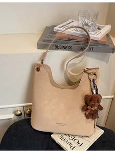 Beige matte Lederschultertasche mit Bärenanhänger auf Sitz neben Kunstbüchern