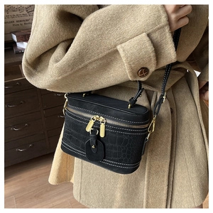 Detailed close-up of a black vanity bag featuring white contrast stitching and crocodile texture