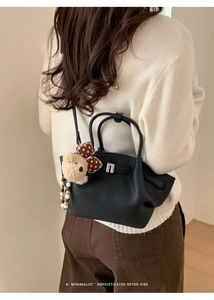 Detail of black pebbled leather handbag with cute plush bear charm and metallic buckle closure