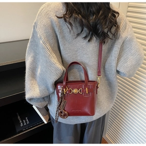 Detail of burgundy leather tote bag with heart buckle and pretzel charm worn with grey sweater