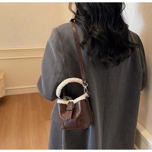 Détail d'un sac seau marron avec bordure en fausse fourrure blanche sur un manteau gris
