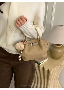 Detail of lychee pattern leather tote with metal clasp and plush puppy charm decor