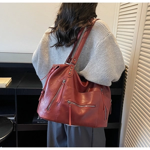 Side view of a large burgundy leather tote bag with multiple zippers worn by a model