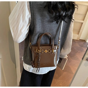 Detail of brown leather bucket bag with gold heart buckle and crossbody strap worn by model
