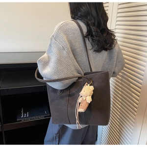 Dettaglio della borsa tote oversize marrone scuro in pelle scamosciata con ciondolo a orsetto