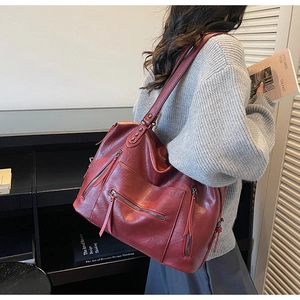 Detail view of large red retro tote bag with functional zippers and long tassels on shoulder