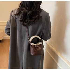 Détail d'un sac seau en cuir marron avec bordure en molleton blanc sur un manteau gris
