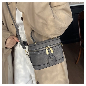 Detailansicht graue Zylindertasche mit Vintage-Textur und weißen Kontrastnähten am Schultergurt