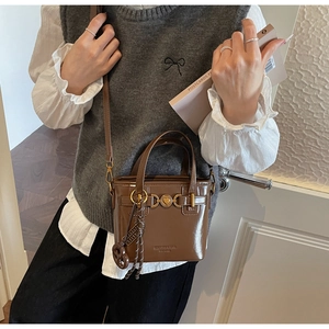 Detail of dark brown glossy leather Boston bag featuring heart logo and woven charm