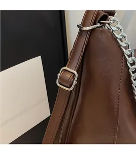 Close-up of brown leather bag strap with silver buckle and metallic chain detail