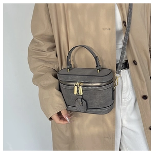 Detail view of dark grey bucket bag with white contrast stitching on khaki trench coat