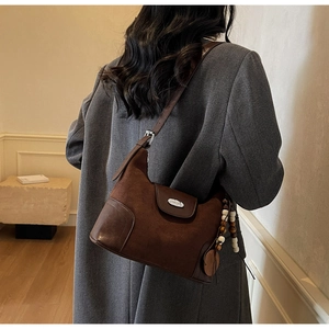 Detail view of brown suede crescent bag with ethnic tassel on a stylish model