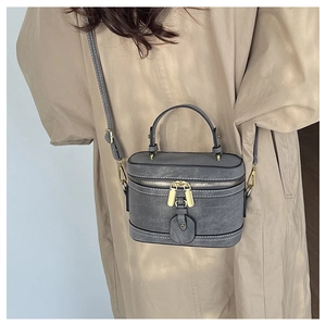 Detailed shot of gray cylinder bucket bag with white stitching and gold hardware on a model