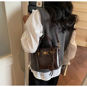 Detail showing the dark brown glossy bucket bag with heart buckle and braided charm accent