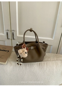 Detail of dark brown lychee leather handbag with silver lock and plush bear charm