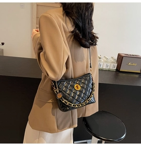 Detail of black quilted leather shoulder bag with gold chain strap and metal clasp closure