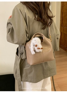 Detail view of a beige leather bucket bag featuring a cute white plush bunny accessory