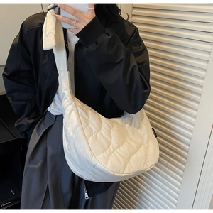 Detail of white quilted crescent bag showing glossy wave pattern and shoulder strap