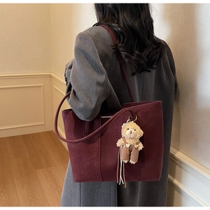 Dettaglio della borsa tote bordeaux con texture opaca e simpatico ciondolo a orsetto