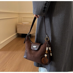 Macro view of brown suede dumpling bag featuring bohemian beaded tassel and metal clasp