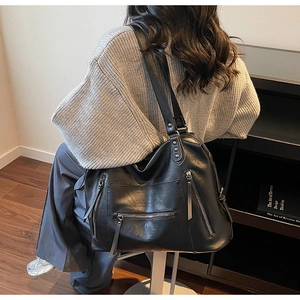 Detail of a large black PU leather tote bag with silver rivets and zippers on a model