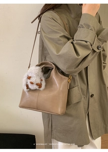 Detail of khaki bucket bag with plush charm on olive trench coat for a retro vibe