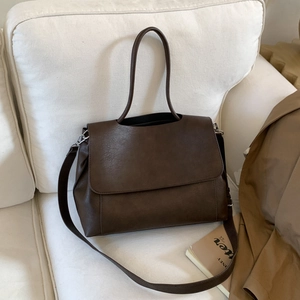 Dettaglio della borsa a tracolla in pelle PU marrone scuro su divano con vari accessori