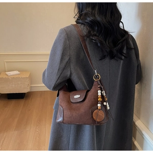 Detail of dark brown dumpling bag with suede texture and bohemian wooden bead pendant