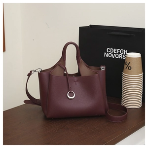 Detail of burgundy lychee leather bucket bag with silver ring charm on dark wood