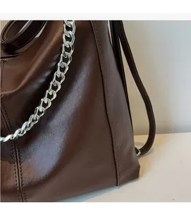 Detail of dark brown leather texture and bold silver metal chain strap on tote bag