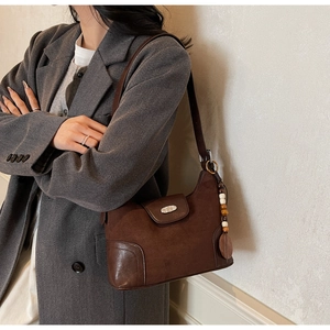 Detail of a dark brown suede crossbody bag showing the leather base and wooden bead charm