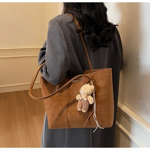 Dettaglio di una borsa tote marrone vintage con ciondolo a forma di orso e tracolla