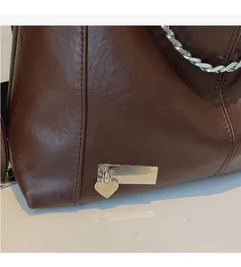 Close-up of brown leather bag featuring silver chain straps and heart pendant detail