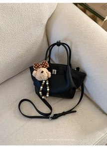 Detail of black lychee grain handbag with cute plush bear pendant on a soft beige sofa