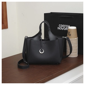 Detailed view of black lychee grain leather tote bag with silver ring on wooden surface