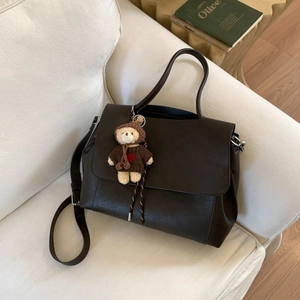 Dettaglio borsa tote marrone scuro in ecopelle con ciondolo a forma di orsetto sul divano