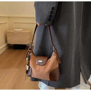 Detail of a brown suede and leather crossbody bag featuring a wooden bead tassel