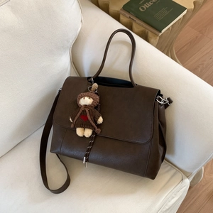 Dettaglio di borsa tote in pelle marrone scuro con ciondolo a forma di orsetto