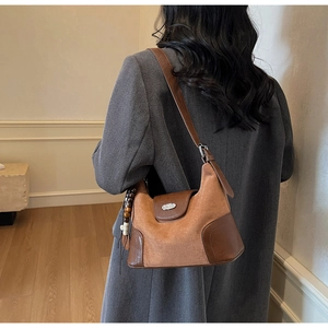 Detail of suede dumpling bag with caramel leather trim and wooden bead charm on shoulder strap