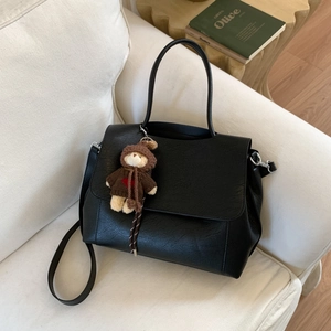 Dettaglio di una borsa tote in pelle nera testurizzata con ciondolo a forma di orso