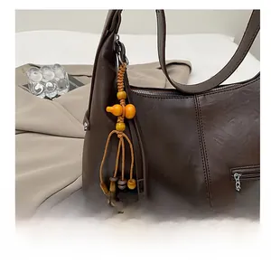 Détail d'un sac à bandoulière en cuir marron avec fermeture éclair et breloque orange