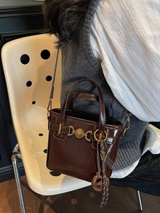 Vintage brown leather bucket bag with gold heart clasp and tassel detail on model