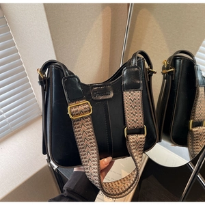 Detail of black bucket bag featuring textured leather and geometric wide strap