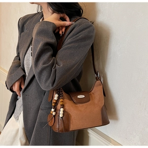 Close-up of brown suede hobo bag with beaded tassel detail worn by model in suit