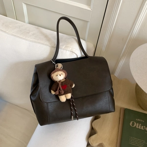 Dettaglio di borsa tote in pelle marrone scuro con ciondolo a forma di orsetto