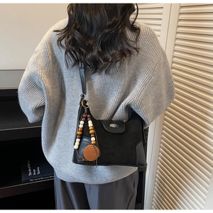 Detail of black suede shoulder bag with retro wooden beads and long tassel charm