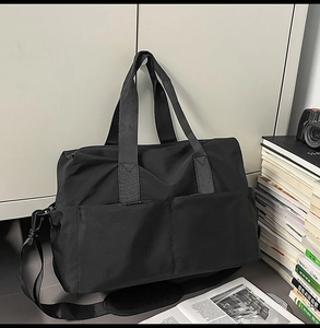 Dettaglio borsa da viaggio nera con manici spessi, tracolla e doppie tasche anteriori