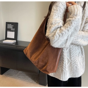 Detail of a large brown suede tote bag styled on model in a minimalist interior